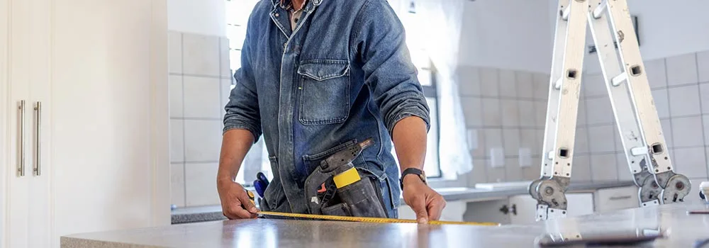 Remodeler measuring a kitchen countertop before pricing the job