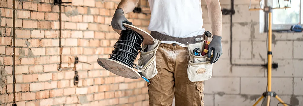 Electrician with a wire spool and loaded tool belt ready for rough-in work