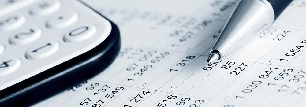 A calculator and pen sit on printed financial statements, the manual double entry contractors face without a QuickBooks integration