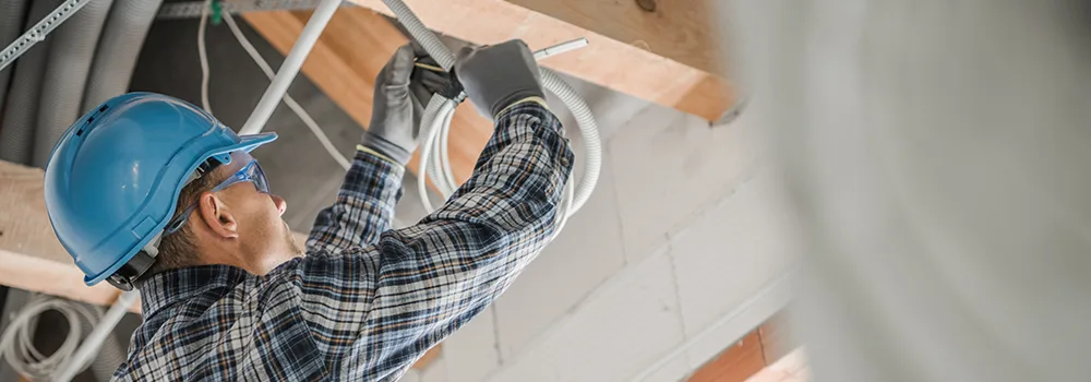 An electrician works in an electrical panel; hours like these are real job costs, and time tracking is how they make it onto the invoice