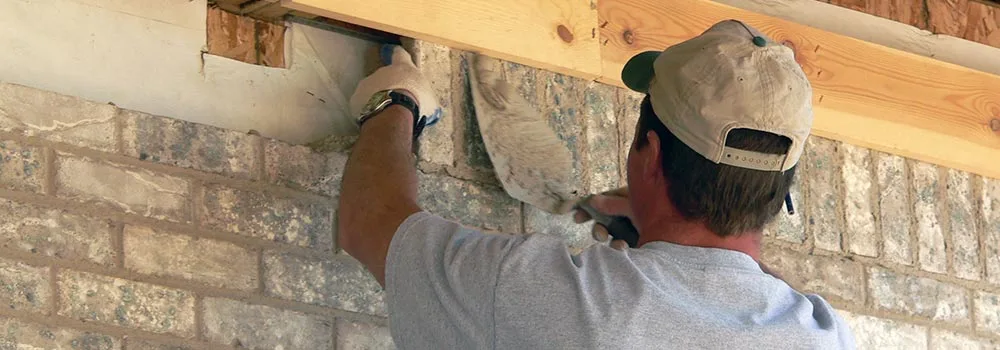 A mason works on a brick wall beneath new framing; code crew time at the level you bid, like masonry by phase, and stop there