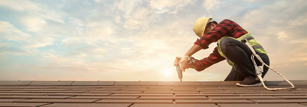 A roofer fastens roof tiles as the sun sets; under both methods you bill for completed work like this, the difference is the paperwork